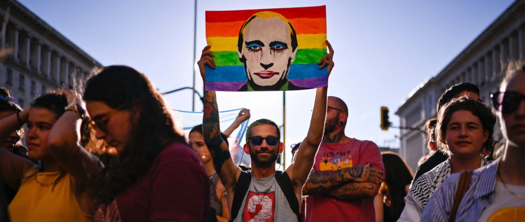 A protester holds a portrait of Russia's President Vladimir Putin against a Rainbow flag during a demonstration against a new law banning LGBTQ "propaganda" in schools in Bulgaria, in Sofia on August 07, 2024. Bulgaria's parliament passed changes to its education law on August 7, 2024 widening its scope to ban LGBTQ "propaganda" in schools in what rights groups slammed as "discriminatory". The amendment to the law, proposed by the country's pro-Russian Vazrazhdane party, passed by a large majority, with 159 votes in favour, 22 against and 12 abstentions. The law now bans the "propaganda, promotion or incitement in any way, directly or indirectly, in the education system of ideas and views related to non-traditional sexual orientation and/or gender identity other than the biological one". (Photo by Nikolay DOYCHINOV / AFP) (Photo by NIKOLAY DOYCHINOV/AFP via Getty Images)